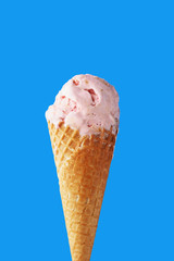 Pink ice cream in a waffle cone on a light blue background. Close-up