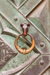 A brass knocker in the shape of a ram's head on a door, detail of iron door