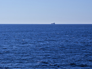 Distant cargo ship sailing at textured sea.