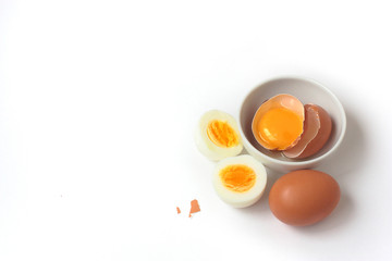 Brown eggs (1 whole raw egg, 1 broken egg in a small plate, 1 hard boiled egg). White background, day light, space for text on the left. Objects on the right.