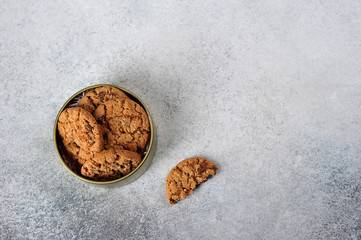 Chocolate Chip Cookies in a round box. Near the box is a half cookie. View from above. Light background. Free space for text.