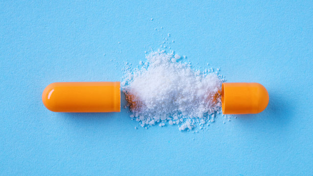 Close Up Split Open Medical Pill Capsule With Spilled White Powder On Blue Background