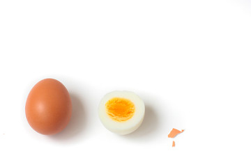 Two eggs in line (1 whole brown egg and а half of a hard boiled egg). Small piece of shell. White background, day light, space for text.