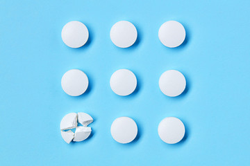 Round white medical pills arranged in square order and one of them is crushed into four parts. Pill splitting.