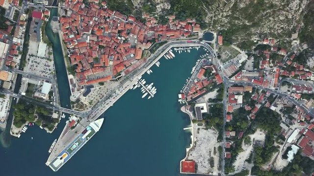 Overhead aerial view of rooftops and streets in historic old town of Kotor and Dobrota and bay for liner and boats in Montenegro in 4k