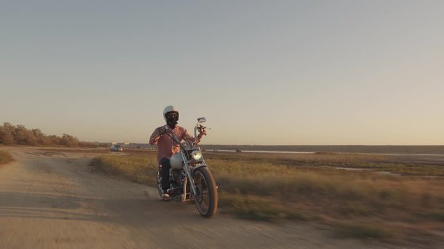 Young stylish motorcyclist driving his motorbike in the desert road during sunset 