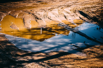 Deep spring puddle on the sandy road due to melting snow after winter.