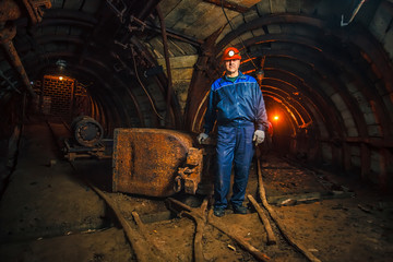 A miner in a coal mine stands near a trolley. Copy space.