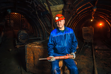 A miner in a coal mine stands near a trolley. Copy space.
