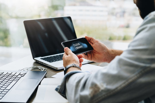 Man sits in cafe, uses smartphone with inscription on screen- cloud library. Man is looking for information in cloud library.