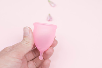 Female hand holds a menstrual cup over pink background. Women's health concept, alternative to...