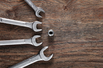 Metal wrenches directed towards a heaxgon nut on wooden table.