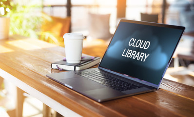 Close up of laptop with inscription on monitor- cloud library and paper cup of coffee on in empty cafe. Workplace without people.