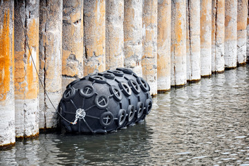 Big black rubber buoy fender covered with car tires floating on the water at the harbor