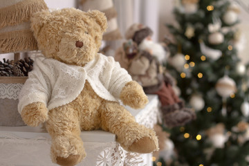 Close-up toy Teddy bear on a mantelpiece on a blurred background of a decorated Christmas tree, selective focus