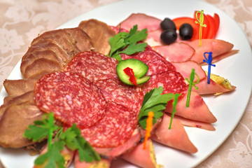 Meat slices with greens, olives and vegetables on a white plate, close-up