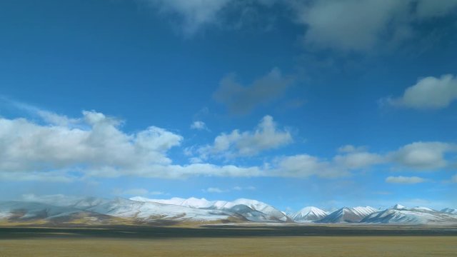 Train window offers a beautiful vista of the plains and the snow covered mountains in Tibet. Breathtaking view of white clouds drifting over the empty plains and snowy Himalaya during a train ride.