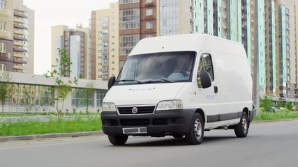 Tracking shot of white delivery van driving along road in city