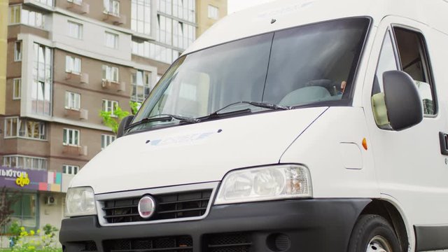 Tracking shot of white mail delivery van driving along road in city