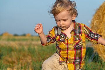 Little fair-haired boy playing on a wheat field with bales
