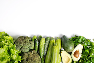 Bunch of greens and herbs laid on white countertop. Halved avocado, lettuce salad leaves, raw broccoli and other vegetables in row. Vegan diet concept. Close up, copy space, background, top view.