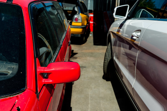 An old red passenger car is standing on the site of a car repair shop. Nearby is a new white modern car.
