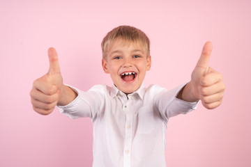 Portrait of little adorable boy having fun and smiling. Thumbs up. studio portrait over pink background. wearing jeans and white shirt.