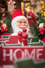 A traditional Santa Claus in red clothes among Christmas items with warm twinkle lights in the background.