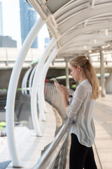 Fototapeta na wymiar Businesswoman Using Phone On Walkway Bridge In City