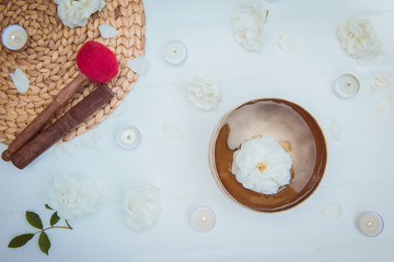Top view Tibetan singing bowl with floating in water rose inside. Special sticks, burning candles, flowers petals on the white wooden background. Meditation and Relax. Exotic massage. Copy space.
