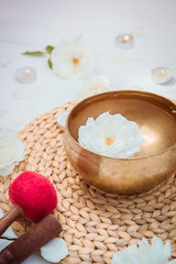 Tibetan singing bowl with floating in water rose inside. Special sticks, burning candles, flowers petals on the white wooden background. Meditation and Relax. Exotic massage. Vertical card. Copy space