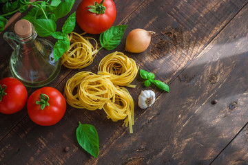 raw ingredients for cooking italian pasta on wooden table top view. fresh tomatoes basil garlic tagliatelle olive oil onion 