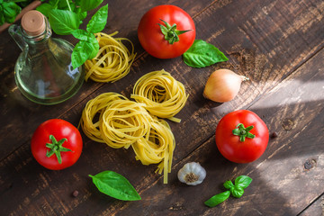raw ingredients for cooking  pasta on wooden table top view. fresh tomatoes basil garlic fettuccine olive oil onion 