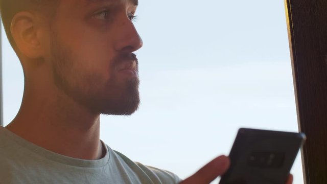 Man looking at his phone near a big window in the office. Warm sunset light is hitting his head. Handheld slow motion shot