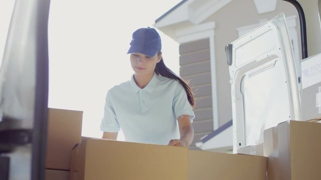 Handheld shot from inside of parked delivery van: young female courier in blue cap checking packages