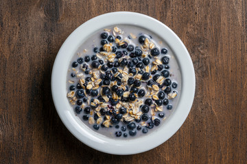 Oatmeal with fresh blueberry, almond milk and honey for breakfast in plate on wooden background. Rustic style. Top view.
