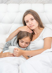 Young mom embracing her little sick girl on the bed at home