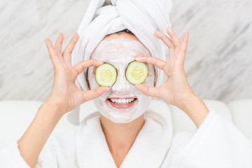 Funny young girl are in bathrobes and with towels on their heads with a mask for skin face and cucumbers on eyes