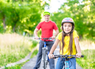 Father and daughter are cycling in the summer park together. Empty space for text