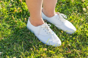 Legs in white sneakers on green grass. View from above. The concept of youth, spring and freedom.