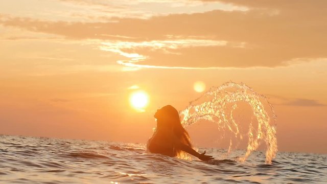 silhouette of a woman tumbling out of the water making a circle with hair with splashes of drops at dawn, a girl swimming in the sea enjoying sunrise, summer vacation concept