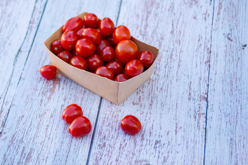 Organic ripe cherry tomatoes in a recyclable paper box on a wooden table. Cooking ingredients. Harvest. Sustainable living. Say “no” to plastic packaging.