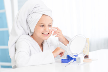 Smiling little girl with a towel on her head with patches on face looks in the mirror