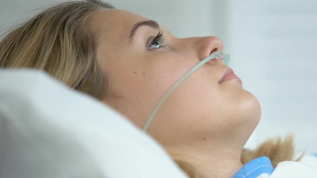 Female hospital patient with nasal cannula lying bed, oxygen therapy, recovery