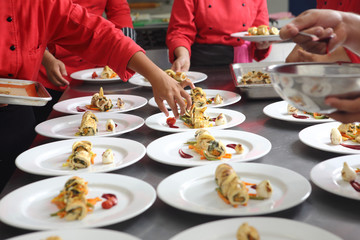 The hands of chefs prepare various dishes for a banquet that includes roasted chicken fillet and dessert. - Powered by Adobe