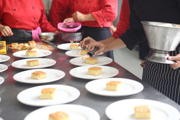 The hands of chefs prepare various dishes for a banquet that includes roasted chicken fillet and dessert.