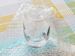 Thick bottom glass half packaged with transparent bubble wrap on a checkered tablecloth. Material...