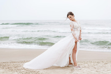 Fototapeta na wymiar positive bride runs on the sea beach on an overcast day