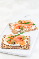 Sandwich with smoked salmon and cream cheese on thin multi seed  crispbread, garnished with green onion and olives, vertical, copy space