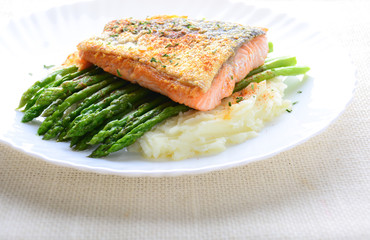 Grilled salmon garnished with asparagus and herbs and mashed potatoes, served on white plated.